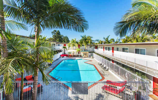 Outdoor swimming pool with sun chairs, a lounge area lined with apartments, and palm trees at Pacific Sands, San Diego, CA