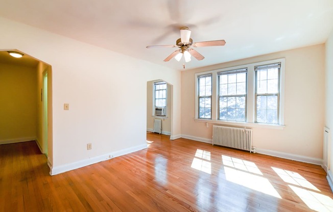 vacant living area with hardwood flooring, ceiling fan and large windows at 3101 Pennsylvania apartments in washington dc