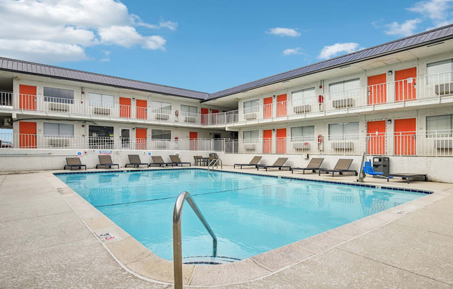 A swimming pool is surrounded by sun loungers in a sunny courtyard.