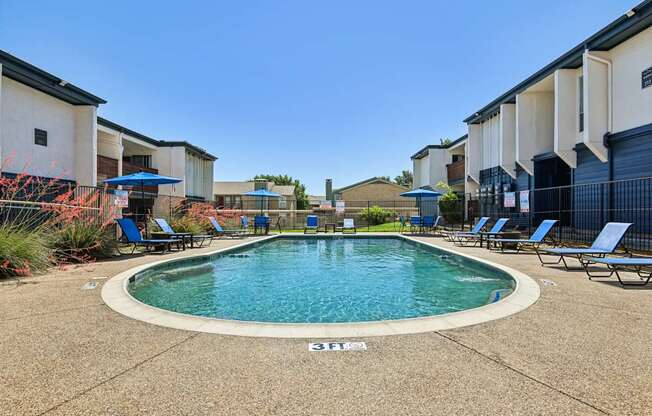 A swimming pool surrounded by lounge chairs in a residential area.