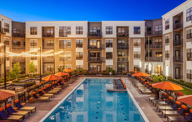 an outdoor pool with lounge chairs and umbrellas in front of an apartment building
