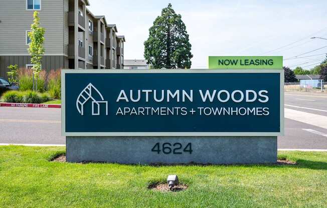 A sign for Autumn Woods Apartments and Townhomes is displayed in front of a building.