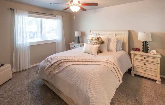 A bedroom with a large bed, a nightstand, and a window with curtains.