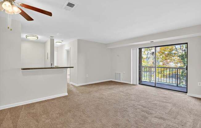 A spacious room with a ceiling fan and sliding glass doors leading to a balcony.