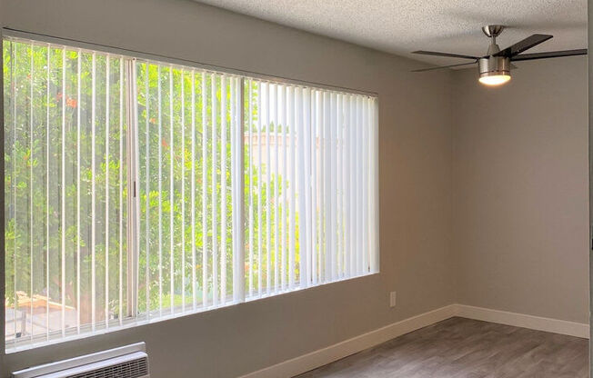 an empty living room with a large window and a ceiling fanat The Arches Apartments, LLC, El Cajon