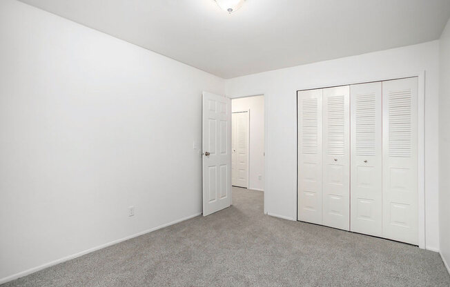 an empty bedroom with white closets and carpeting