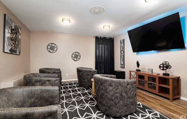A living room with a large grey chair in the center and a flat screen TV mounted on the wall.