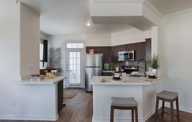 A kitchen with white cabinets and a white island with two stools.