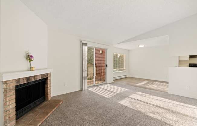 A Pointe East Apartments living room with carpet, a brick fireplace, access to a balcony, and a view of the dining room behind.