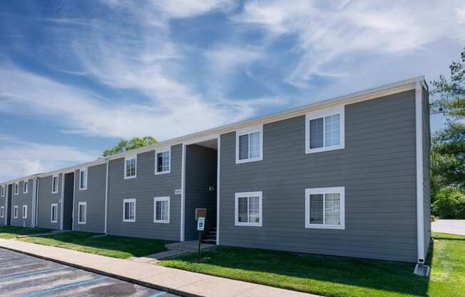 a gray apartment building with a sidewalk and grass
