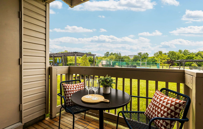 A balcony with a table and chairs overlooking a green field.