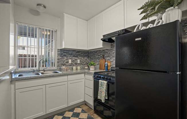 A black refrigerator is in the corner of a kitchen with white cabinets.