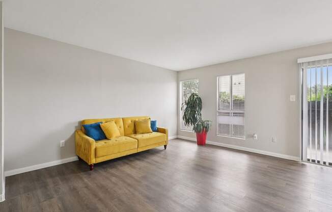 A yellow couch with blue pillows sits in a room with a plant in a red pot.