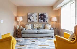 A living room with a grey couch, yellow chairs, and a large painting on the wall.
