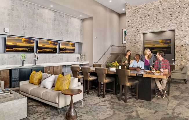 A group of people are sitting around a table in a room with a stone wall and pictures on the wall.