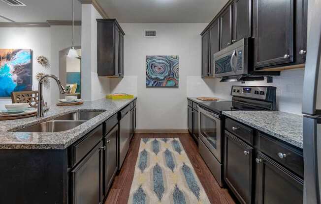 A kitchen with black appliances and a patterned rug on the floor.