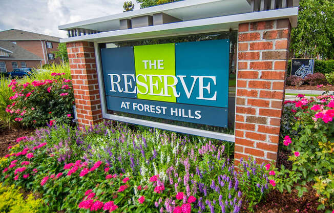 A sign that says "The Reserve at Forest Hills" in front of a flower bed.