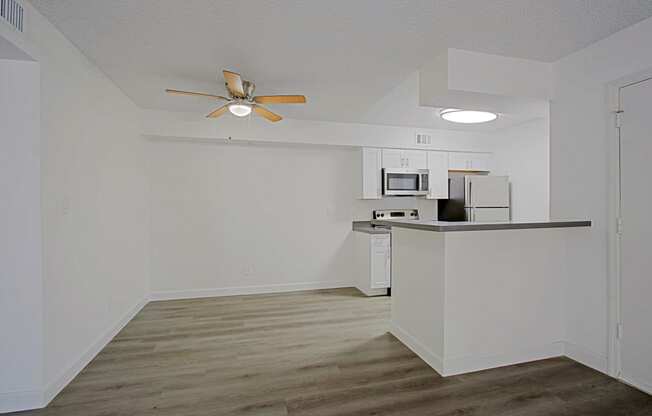 an empty apartment with a kitchen and a ceiling fan