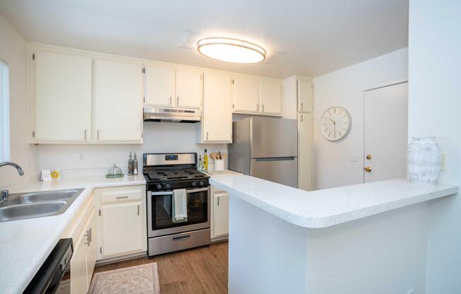 Bright and modern kitchen featuring white cabinets, stainless steel appliances, and a spacious countertop. A large circular light fixture illuminates the area, while a clock adorns the wall. The setup includes a double sink and a cozy rug on the floor, creating a welcoming atmosphere.