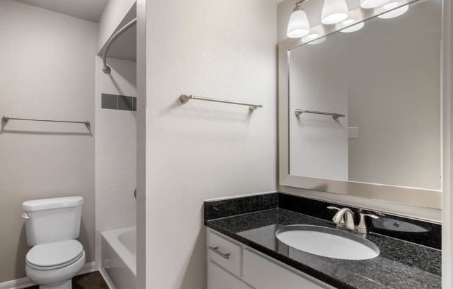 Bathroom with granite countertops, toilet, white shower tiles in shower with bathtub and towel bars.
