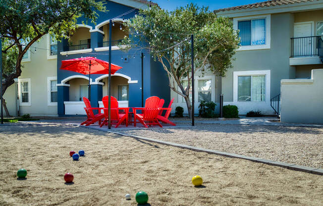 a playground with red chairs and umbrellas in front of an apartment building