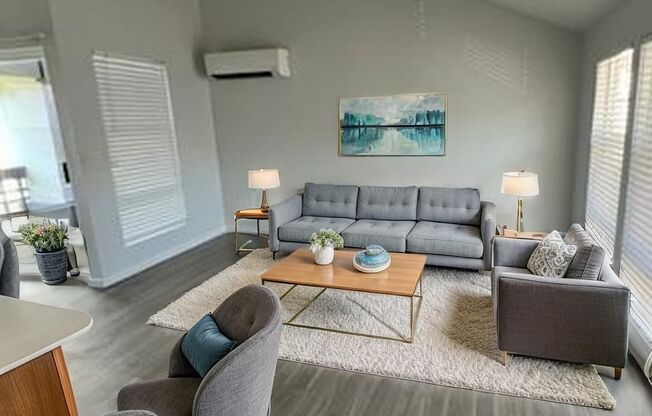 A living room with a grey couch, a grey chair, a wooden table, and a painting on the wall.