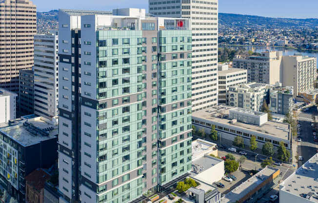 A tall building with a red logo on the side is surrounded by other buildings.