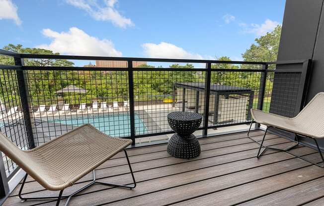 a balcony with two chairs and a table and a pool in the background