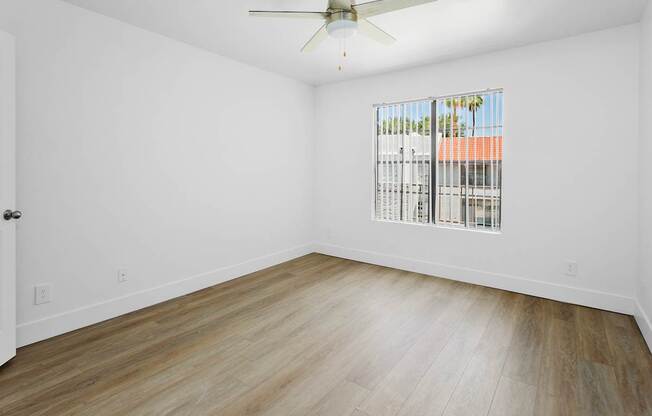 A room with a ceiling fan and a window showing a view of a building.