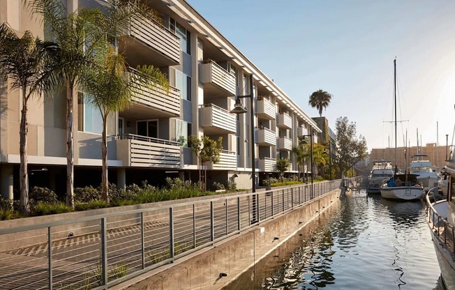A row of modern buildings line a canal with boats docked at the marina.
