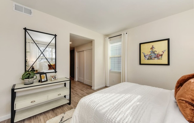 Master bedroom with white bed and copper colored throw pillows, Black and white dresser with mirror positioned above it at Morgan Ranch Apartments, Morgan Hill