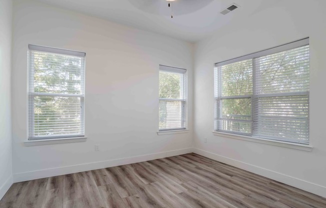 an empty room with two windows and wood floors