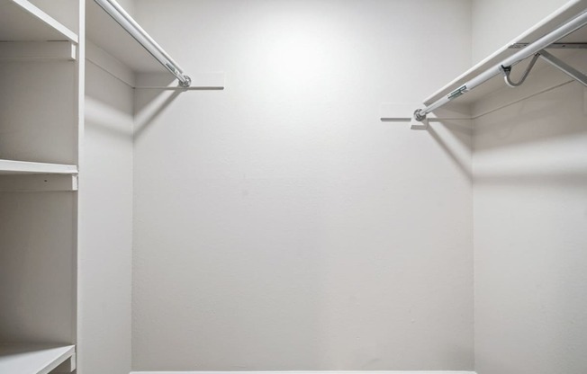 an empty walk in closet with white walls and white hangers