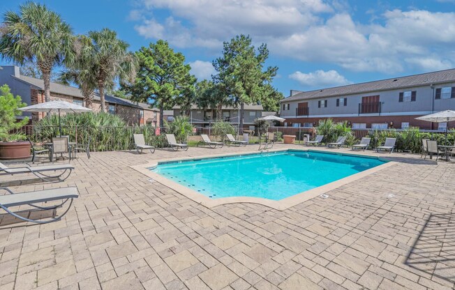 A pool surrounded by a brick patio and lounge chairs with umbrellas at Magnolia Apartments in Shreveport, LA
