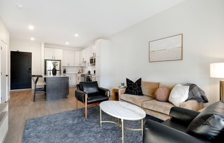 A living room with a black leather couch, a white coffee table, and a grey rug.