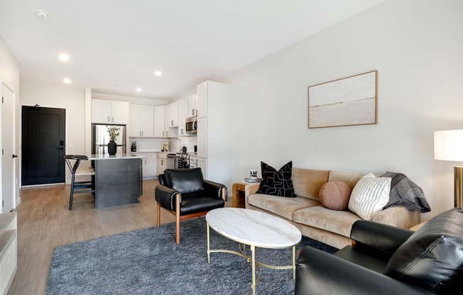 A living room with a black leather couch, a white coffee table, and a grey rug.