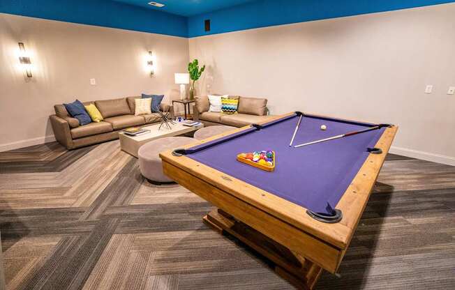 A pool table in a room with a couch and a plant.