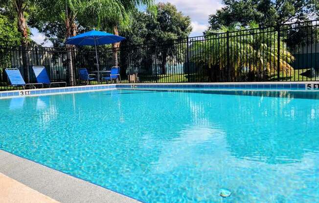 a swimming pool with a blue umbrella and chairs