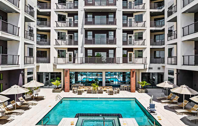 A large swimming pool in the middle of a courtyard surrounded by chairs and umbrellas.