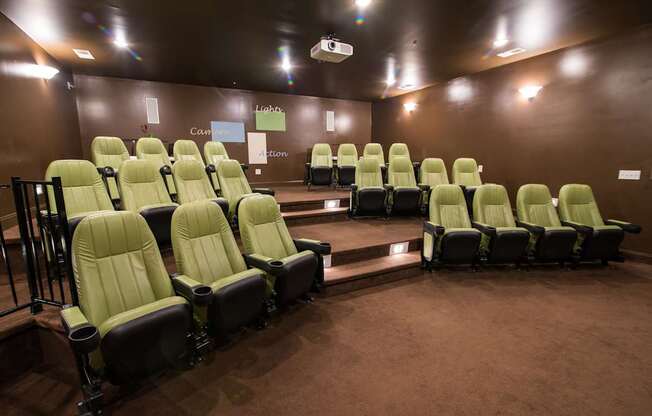 A row of green cinema seats are empty and facing a screen.