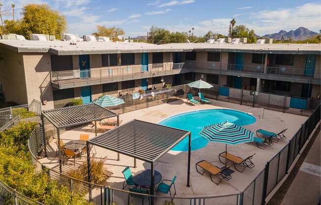A pool surrounded by chairs and umbrellas in front of a building.
