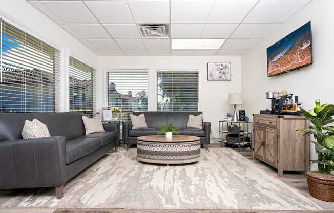 A living room with a grey couch, a coffee table, and a large window with blinds.