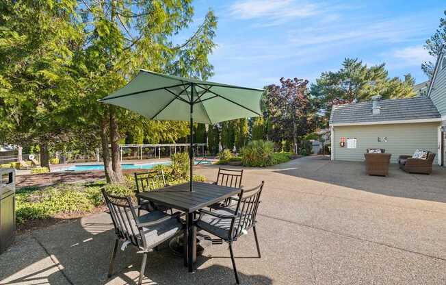 A table with two chairs and an umbrella is in the foreground of a pool at Clackamas Trails Apartments, Oregon, 97222
