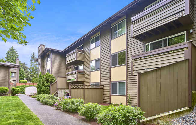 Exterior view of personal patios or balconies, manicured grounds and building, and blue skies in the background at Heritage Grove, Renton, WA.