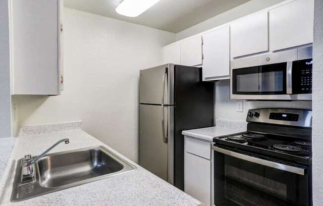 A kitchen with a black refrigerator, stove, and microwave.