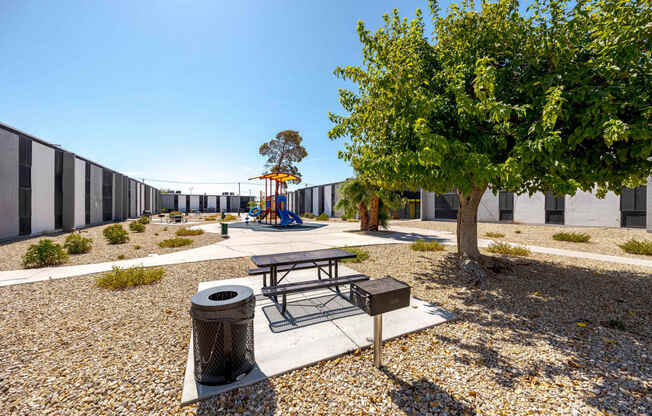 a playground with a picnic table and a tree in front of a building