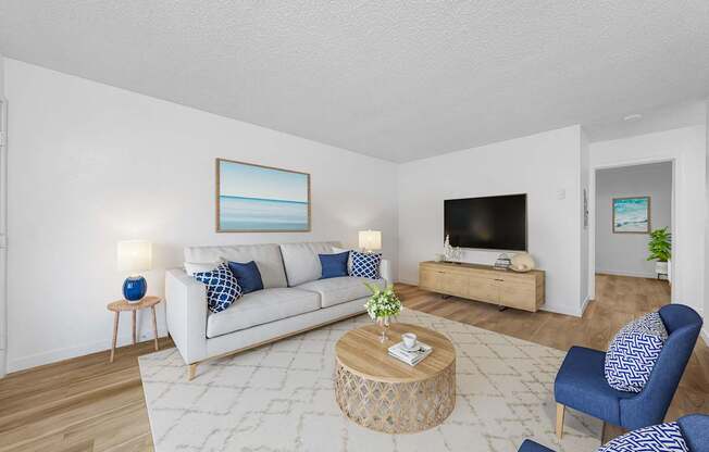 A living room with a white couch, blue chairs, and a painting on the wall.