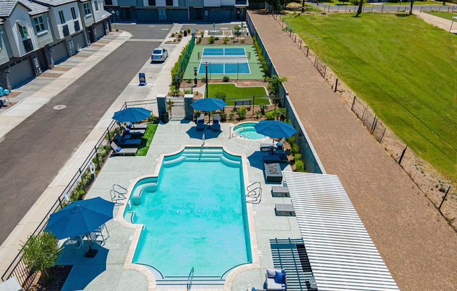 A large swimming pool surrounded by a metal fence and a small tennis court.