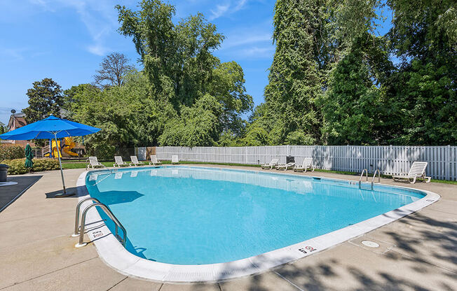 a swimming pool with chairs and an umbrella in a yard