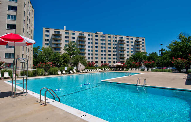 A swimming pool with a red umbrella and a building in the background.